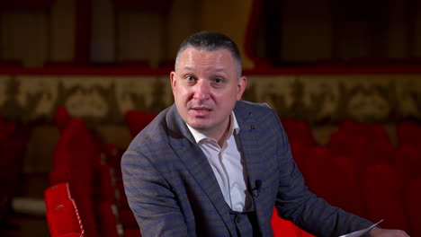 portrait of an actor during the rehearsal. man in suit sitting in a theater hall and performing a monologue while holding a script.