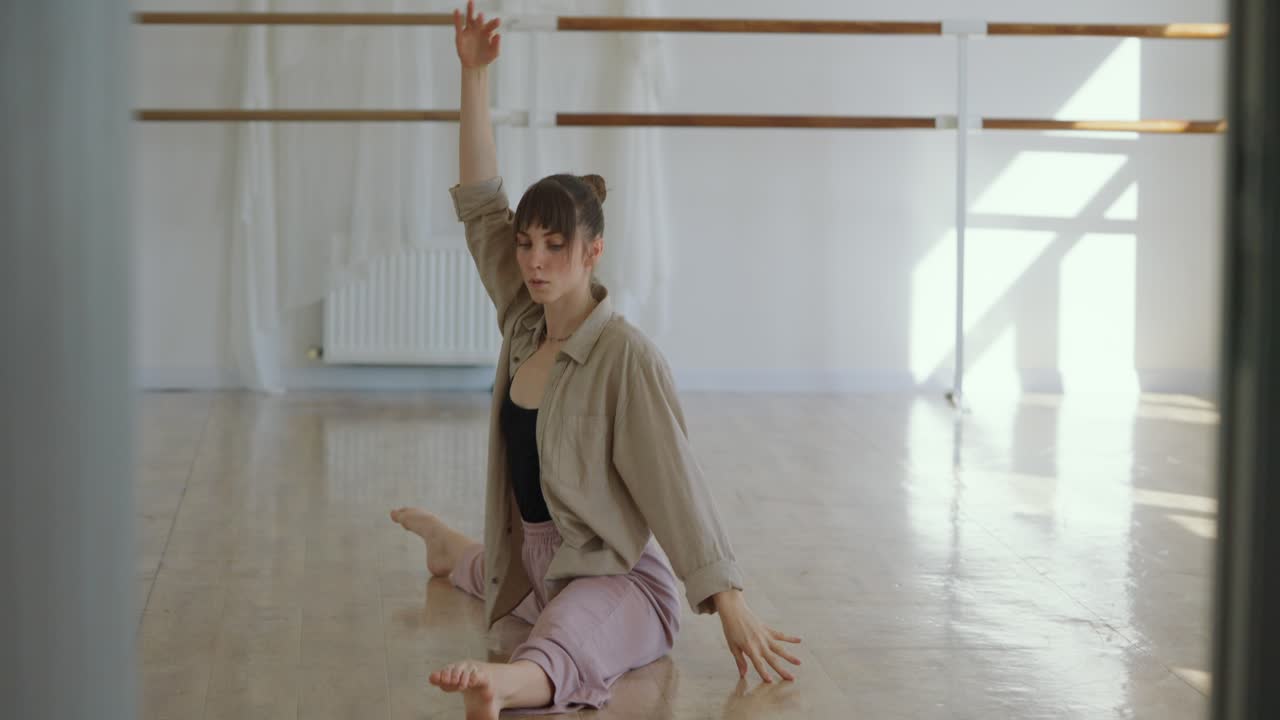 Young woman practices stretching splits in a dance studio