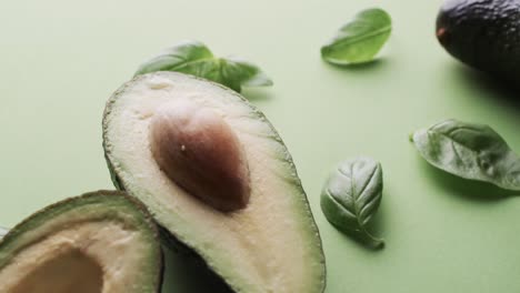 video of sliced avocado and basil leaves with copy space over green background