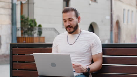 man using laptop having video call chat conversation for online meeting on urban city street bench