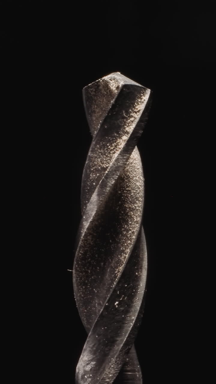 Twisted drill for wood with dirty tip in shavings illuminated with bright studio light. Effective tool for woodwork on black background macro