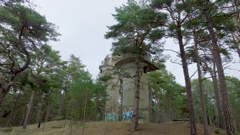 Establishing-aerial-view-of-old-Soviet-military-concrete-observation-watchtower,-pine-tree-forest,-Liepaja-,-military-heritage,-Nordic-woodland,-wide-drone-dolly-shot-moving-forward-low