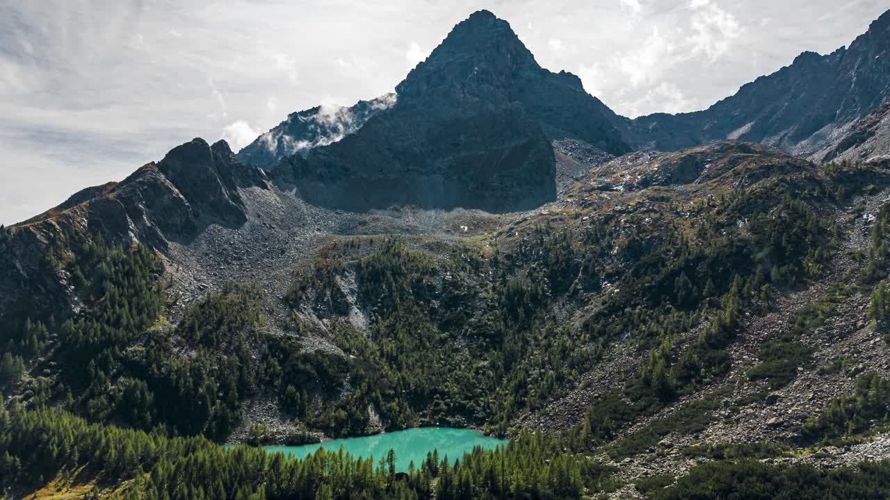 Veduta aerea che mostra un lago turchese cristallino incastonato tra montagne rocciose e foreste verdi. Hyperlapse.