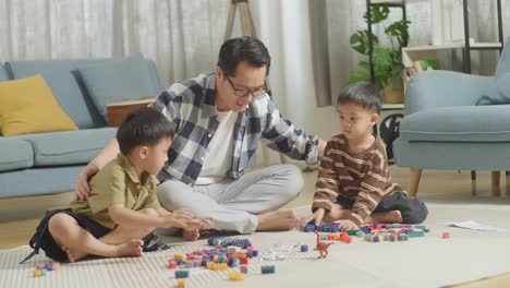 full body of asian father and sons playing the construction set colorful plastic toy brick at home. the father hugging his kids, playing the construction car set plastic blocks, talking and spending time together