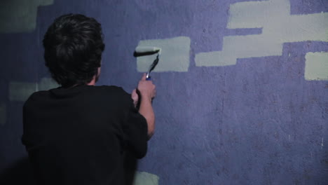 a graffiti artist steadily touches up a brick with a paint roller to form graffiti