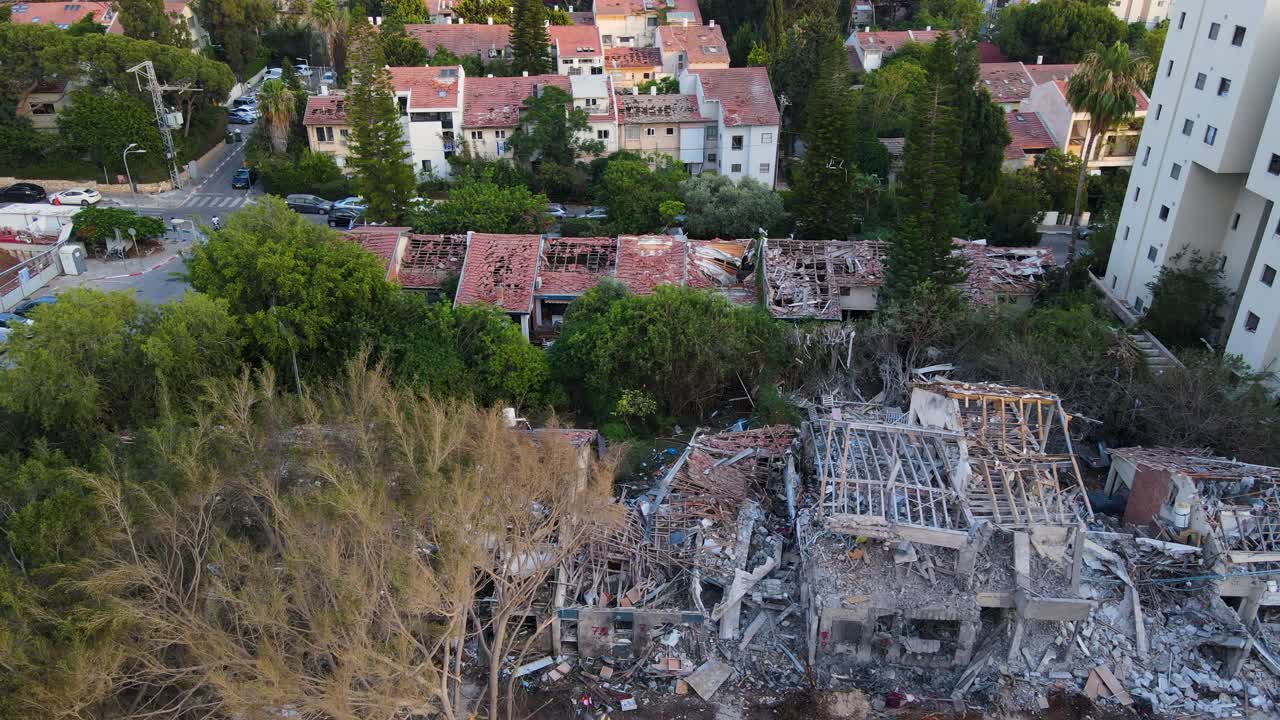 Drone in downward view flies over buildings in Tel Aviv, from a fully destroyed structure to gradually less damaged houses.