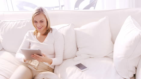 Blonde-Frau-Lächelt-Und-Benutzt-Tablet-Auf-Einem-Sofa