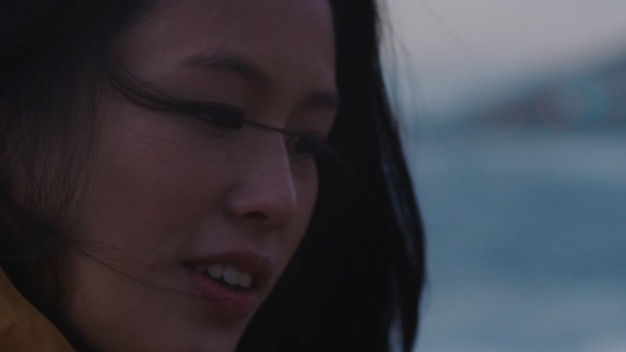 섣달 그믐날을 축하하는 불꽃놀이를 들고 있는 행복한 아시아 여성의 초상화를 닫고 일몰 때 해변에서 독립 기념일 축하를 즐기며 웃고 있습니다