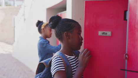 opening locker, girl with backpack organizing books in school hallway