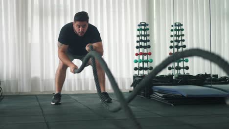 young man using battle ropes for whipping exercise in a gym