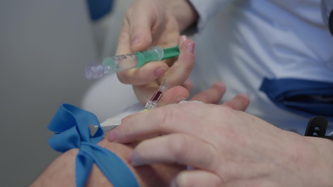 Infermiera guantata fissa una cannula endovenosa sulla mano di un paziente con un laccio emostatico durante il trattamento.