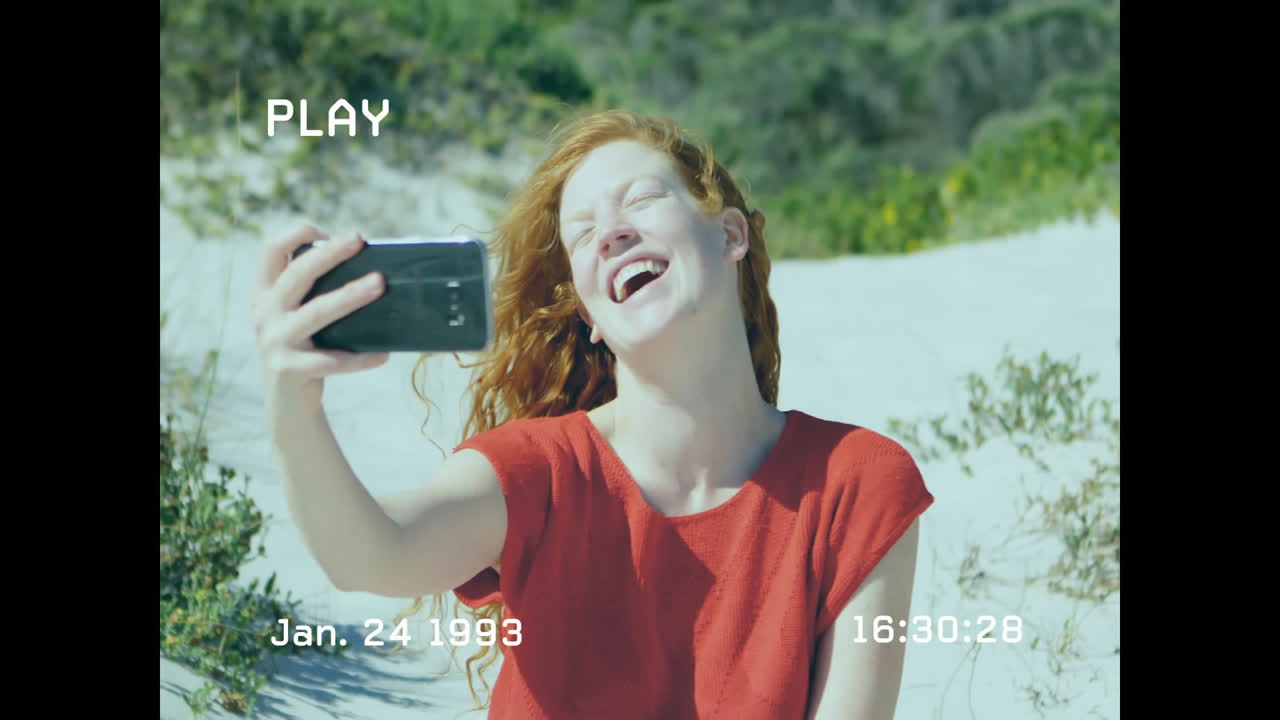 Taking selfie with animation, red-haired woman on sunny beach, joyful expression