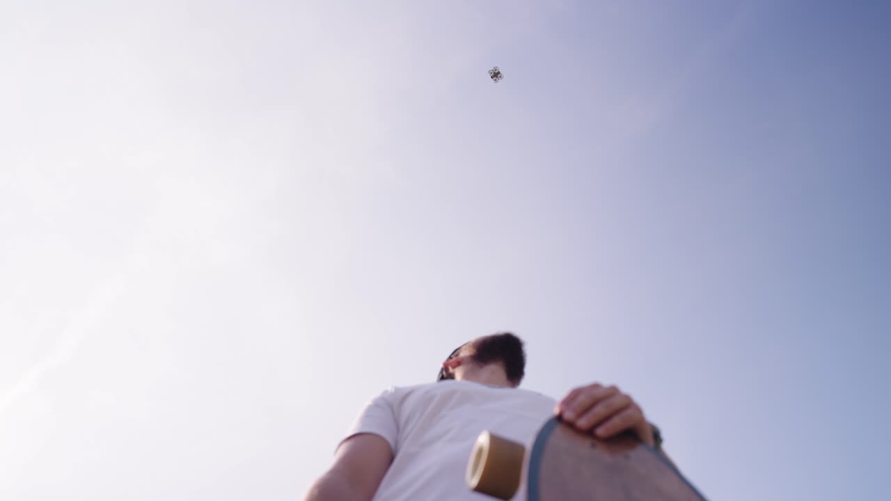 Low angle view of drone hover above bearded male with skateboard, Czechia