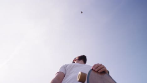 low angle view of drone hover above bearded male with skateboard, czechia
