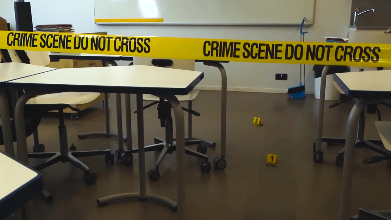 Nastro giallo della polizia che isola un'aula scolastica dopo un grave evento, con segnaposti per le prove sul pavimento accanto a bossoli, a indicare una situazione seria e tragica