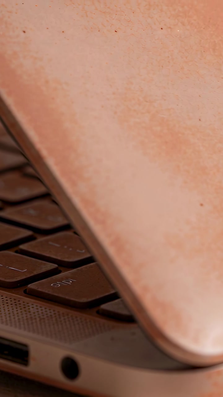 Vertical video: Moving rosegold laptop lid over keys at desk while hinge shifting showing USB port