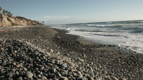 gentle ocean waves roll onto a tranquil shore, framed by scattered pebbles on the sand. soft light and rhythmic surf create a calming, meditative scene perfect for nature and relaxation themes.
