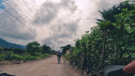 dos ciclistas andan en bicicleta por una carretera dentro de un bosque, una colina y un pueblo en guatemala, américa del norte