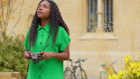 Female-Tourist-With-Camera-On-Vacation-In-Oxford-UK-Exploring-City-Walking-Along-Broad-Street-Taking-Photos-4