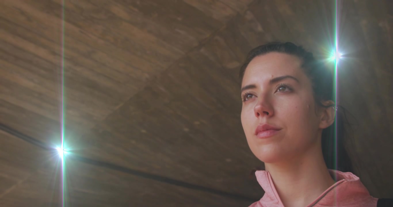 Sunlight streaming, woman breathing under beams, lens flare hitting pink hoodie for wellness