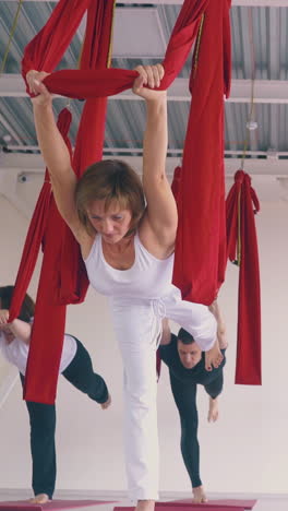 slim young women group enjoys practicing modern fly yoga warrior asana with red hammocks low angle shot close view