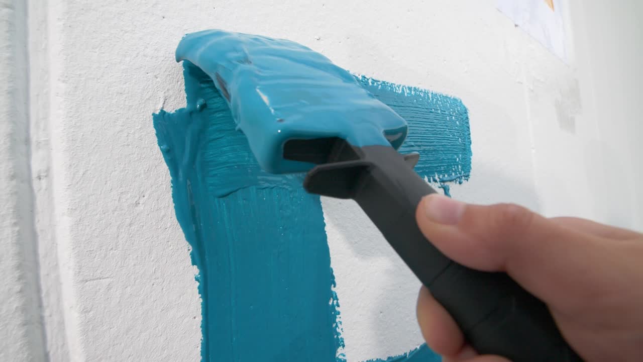 close-up de movimiento lento de la mano de un niño pintando una letra azul en una pared blanca con un pincel de pintura