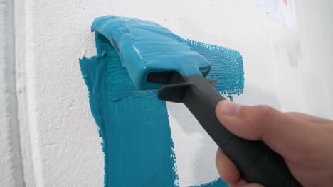 close-up slow motion of a childs hand painting a blue letter on a white wall with a paint brush