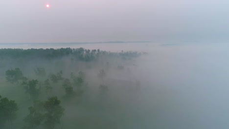 Aerial-view-flying-through-fog-and-smoke-in-a-rural-Alberta-area-towards-a-red-rising-sun-on-a-smoke-filled-horizon