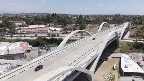 Vehicles-driving-on-6th-Street-Bridge-in-Los-Angeles-as-cross-traffic-moves-along-on-freeway-in-background,-aerial-pull-out