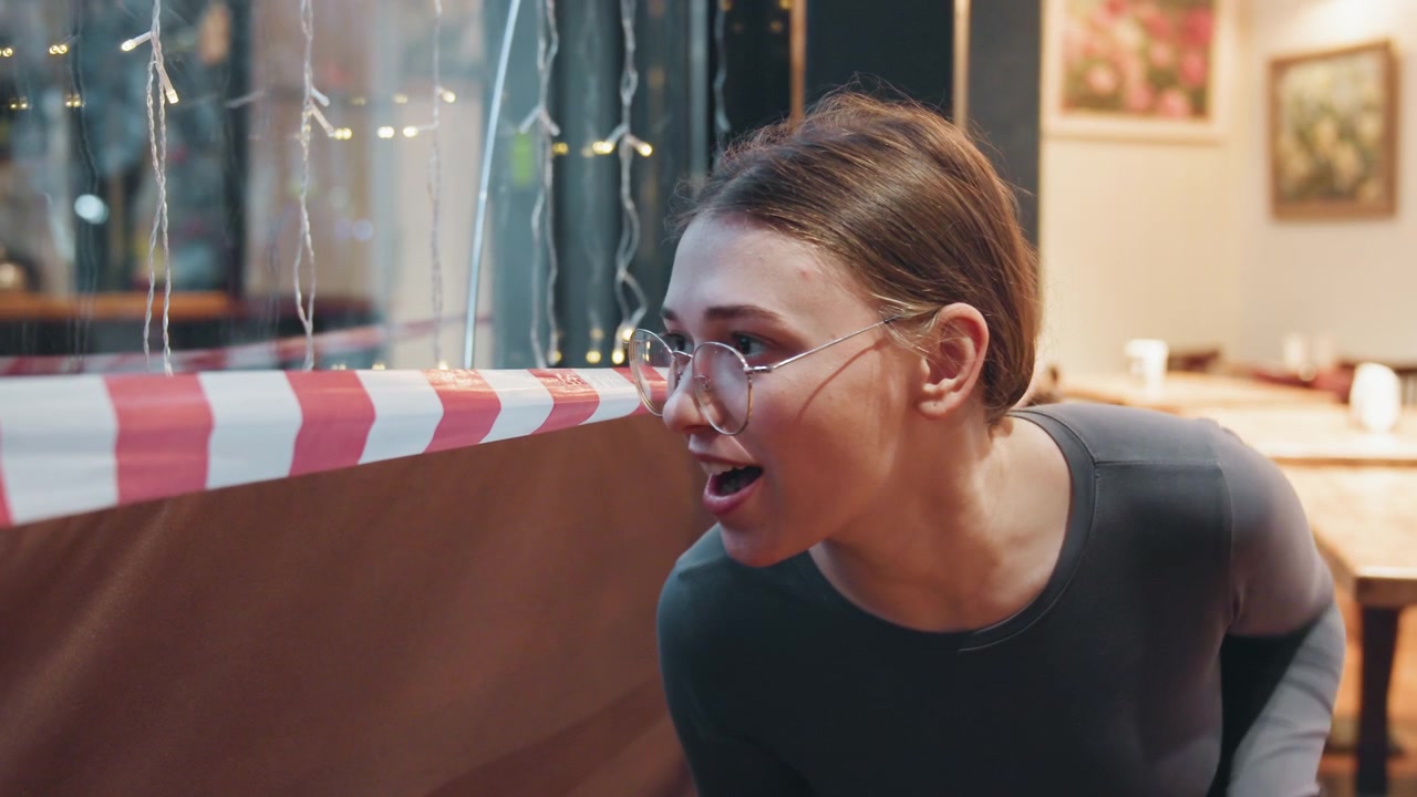 Caucasian woman conversing across caution tape, animated gestures and warm smile, seated at empty cafe booth, cozy lights and interior decor, candid reaction and questioning posture