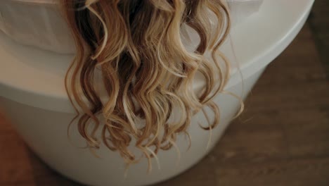 blonde curls cascade over the edge of a white surface, capturing a moment of relaxed beauty