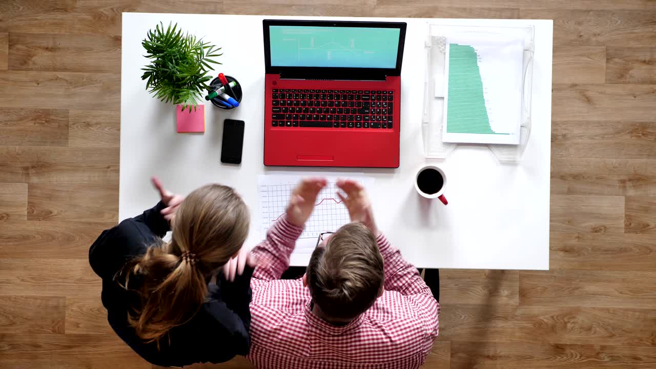 joven con gafas y mujer mirando en la computadora portátil, animando y emocionante, topshot, escritorio con café y documentos