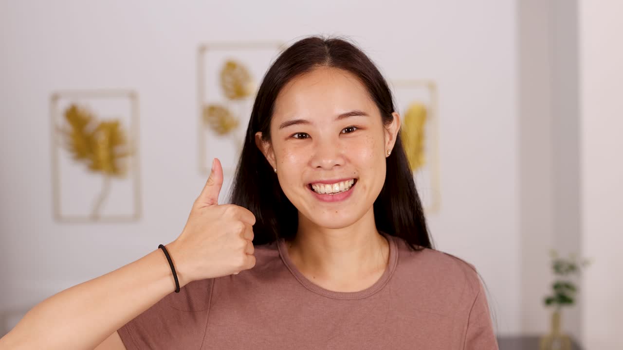 Asian woman smiles and gives thumbs up gesture in bright, cozy indoor home setting