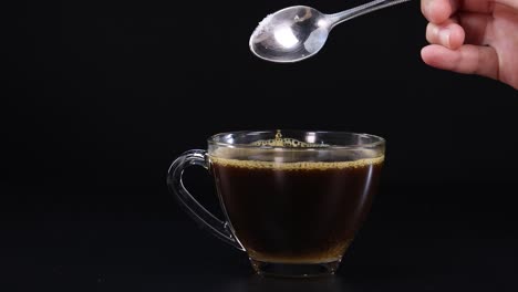 a spoonful of sugar is poured into a glass cup of tea against a black background