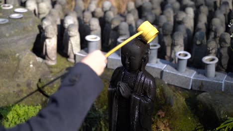 female cleansing a buddha statue with numerous buddha figures in the background - medium shot