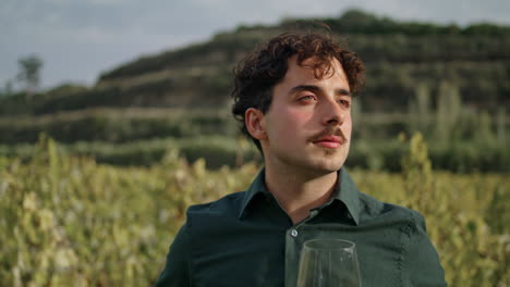 man winegrower looking vineyard holding glass goblet with white wine close up.