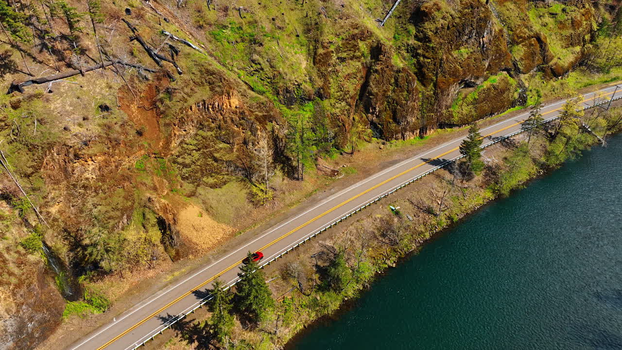 Red car and truck ride by the highway above the mountain river. Steep rocks are on the other side of the road. Top perspective.