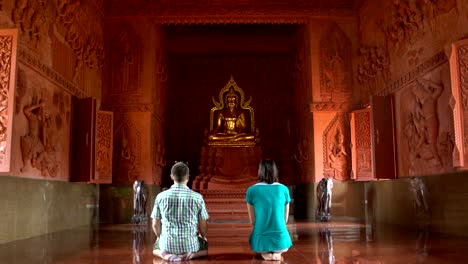 a woman and a man praying while kneeling in front of a buddha statue in a buddhist temple