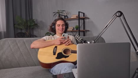 man playing guitar and using phone in home studio