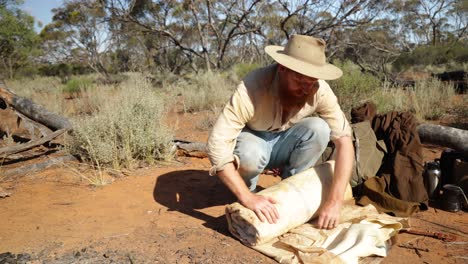 an australian bushman rolls out his authentic vintage oil skin swag in the outback