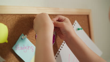 child hands pins bright colourful picture to cork board