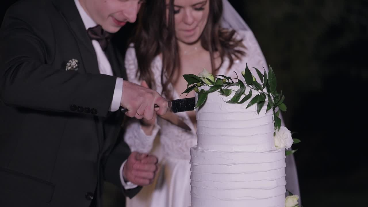Newlyweds cut the wedding cake, lovely bride and groom couple cutting dessert with a knife outdoors