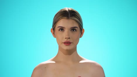 static shot of a young beautiful naked woman licking a heart shaped lollipop while looking sexy into the camera in slow motion against turquoise background in slow motion