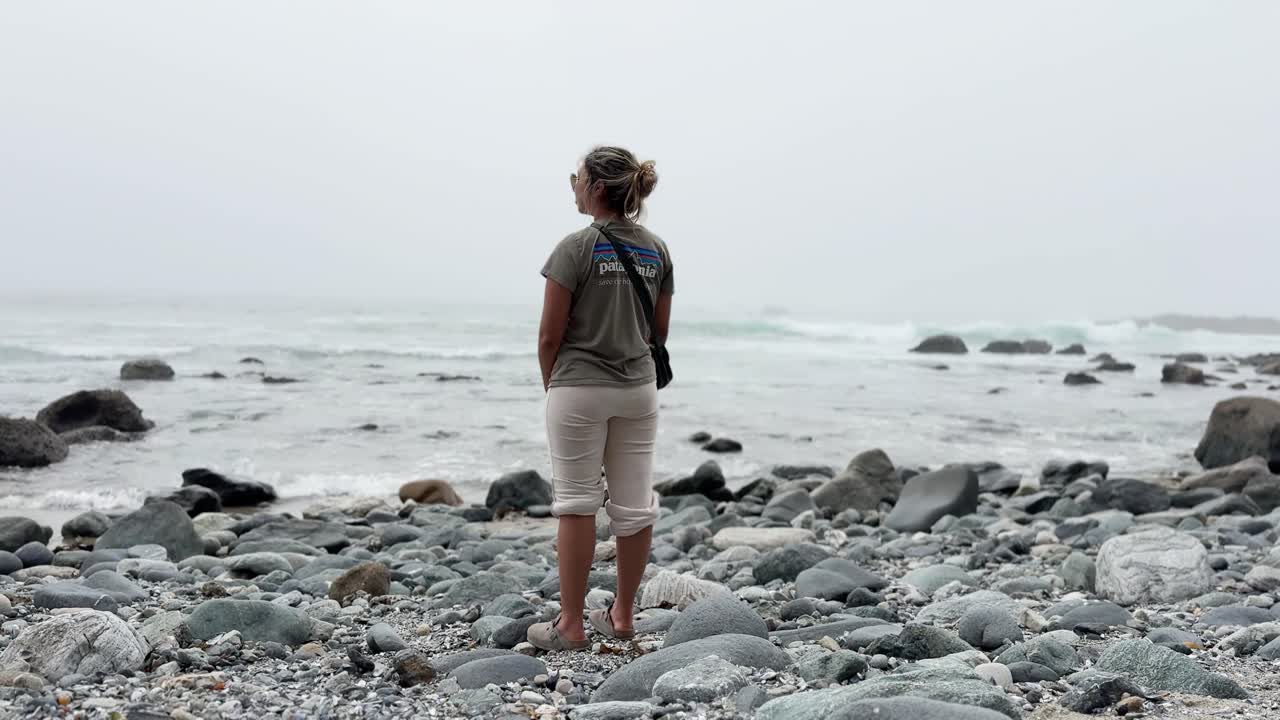 young caucasian traveler standing on a rocky beach in Dana Point California taking in the foggy view wearing sunglasses and rolled up bootleg sweat pants STATIC SHOT