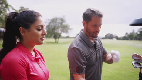 Grupo-De-Golfistas-Masculinos-Y-Femeninos-De-Pie-Junto-Al-Carrito-De-Golf-En-El-Campo-Y-Eligiendo-Palos