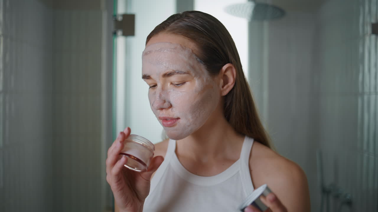 Relaxed girl checking cream bottle at home. Closeup lady with mask