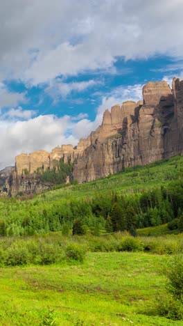 vertical timelapse, clouds and shadpws above steep mountain cliffs and green forest in landscape of colorado usa