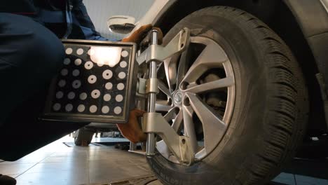 mecánico de automóviles instalando sensor durante el ajuste de la suspensión y el trabajo de alineación de las ruedas del automóvil en la estación de servicio de reparación.