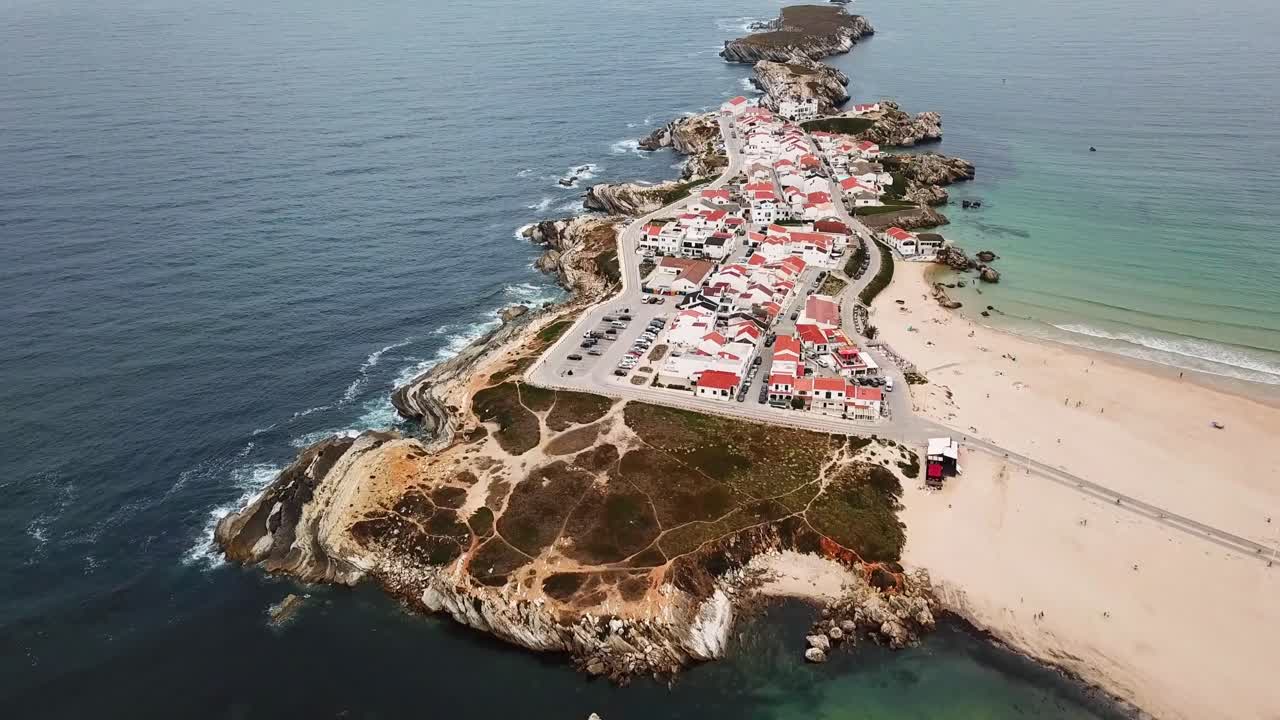 Aerial view of the stunning Baleal peninsula with Praia Norte sandy beache, charming houses, rocky formations, and a sparkling ocean on a sunny day in Peniche, Portugal, drone establishing shot
