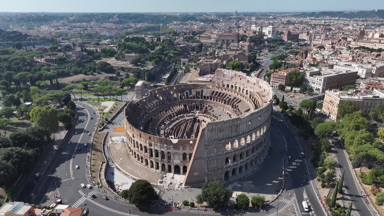 Dronebillede i fugleperspektiv over det antikke Colosseum i Rom, Italien, der viser den omkringliggende historiske by og den travle vejtrafik på en klar og solrig dag